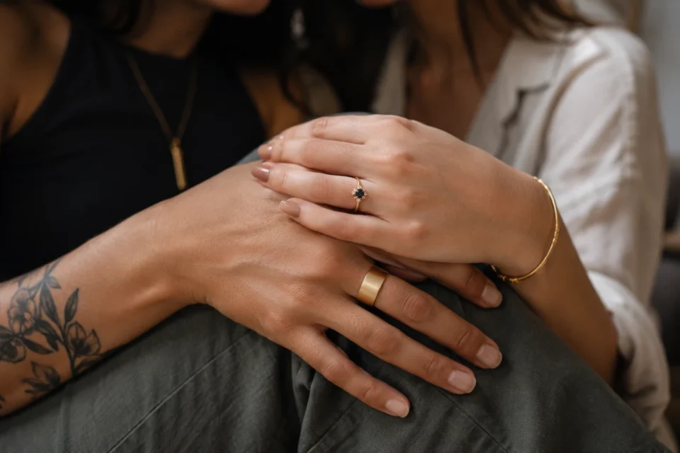 Two women wearing different styles of engagement rings holding hands